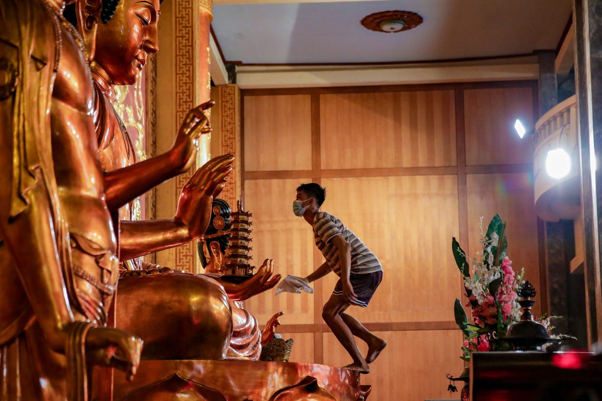 A worker climbs to clean a giant Buddha statue inside a temple in Manila, Philippines. (January 27, 2022)