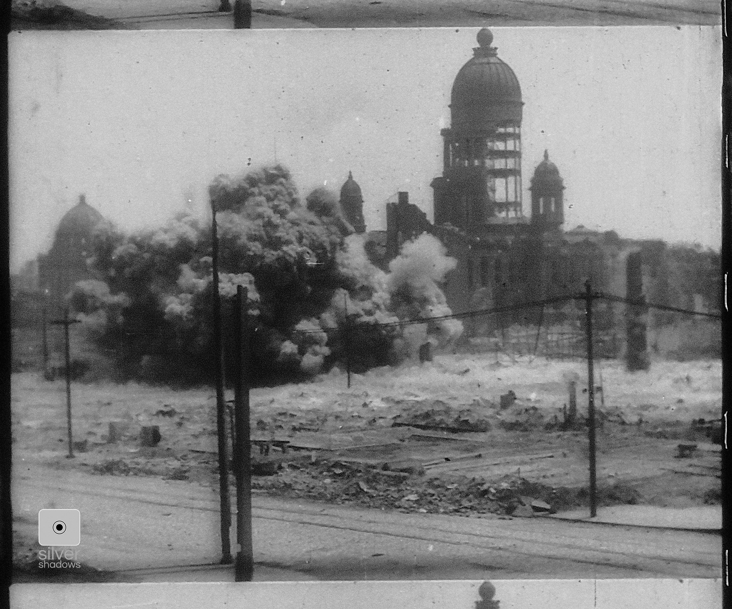 A dynamite blasts in front of the damaged City Hall.
