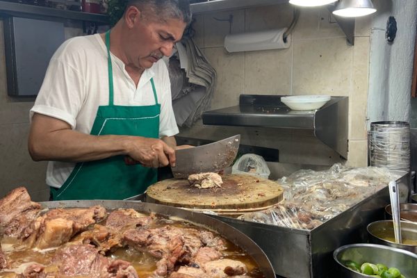A vendor slices up some sesos for a taco next to the vat of meat.