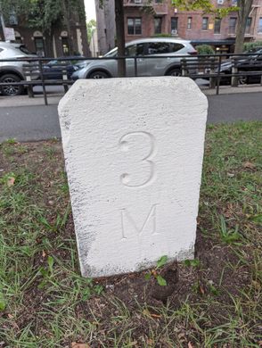 A white stone with "3M" carved into it along a bike path