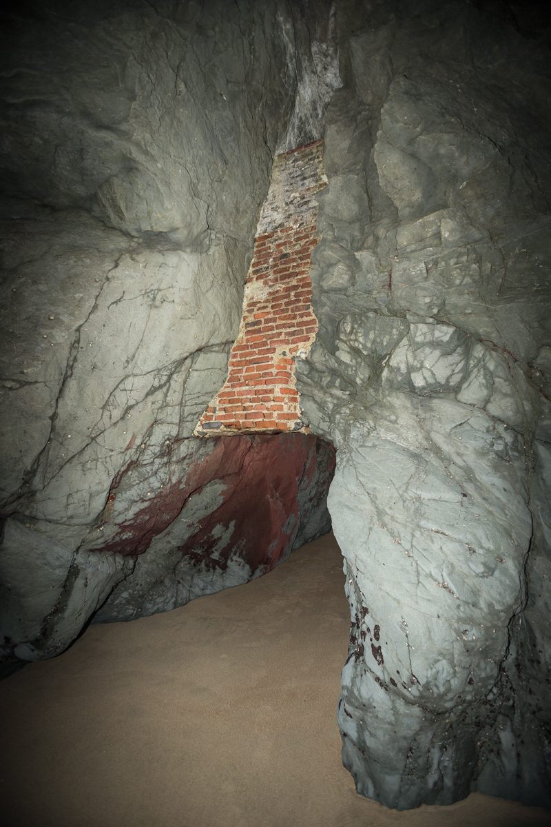 The only access point is a sea cave with remnants of brick and iron infrastructure.