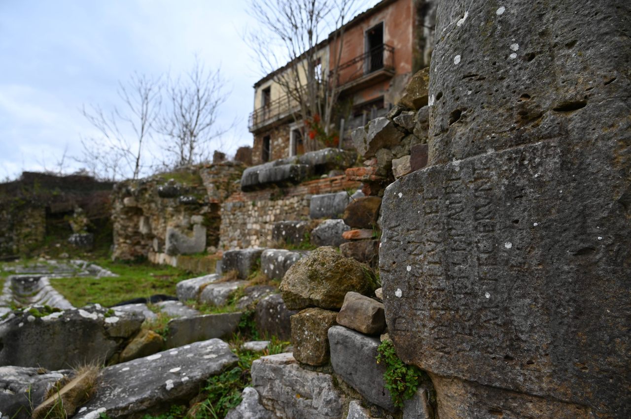 A block carrying an ancient Roman inscription was reused in a medieval wall in Conza. On the left, the remains of the Roman forum can be seen below street-level buildings that survived a 1980 earthquake. 