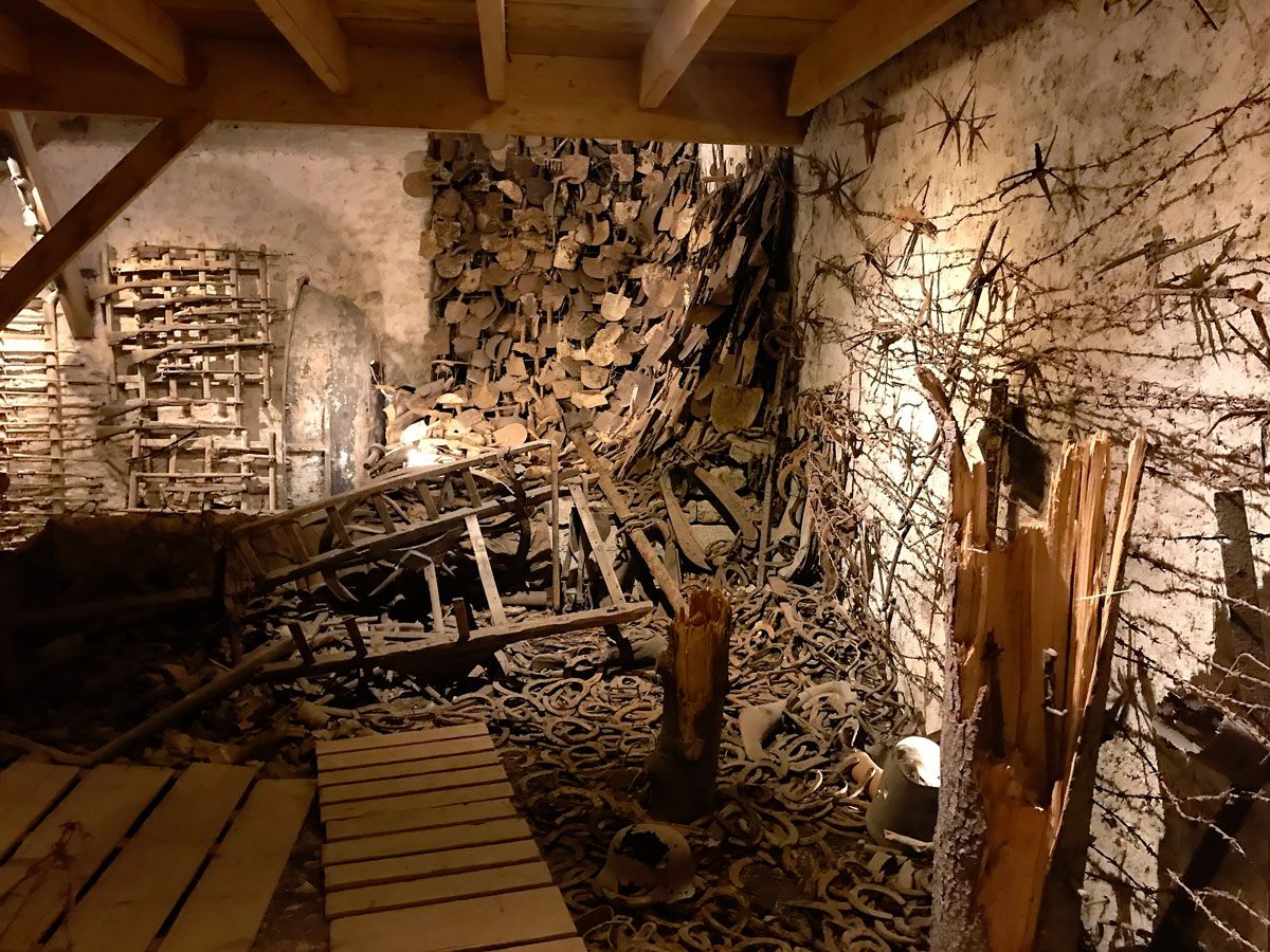A corner installation shows a cascade of rusted shovels, barbed wire, and piles of horseshoes found nearby.