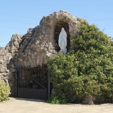A statue of Mary stands in a grotto to the left of the church