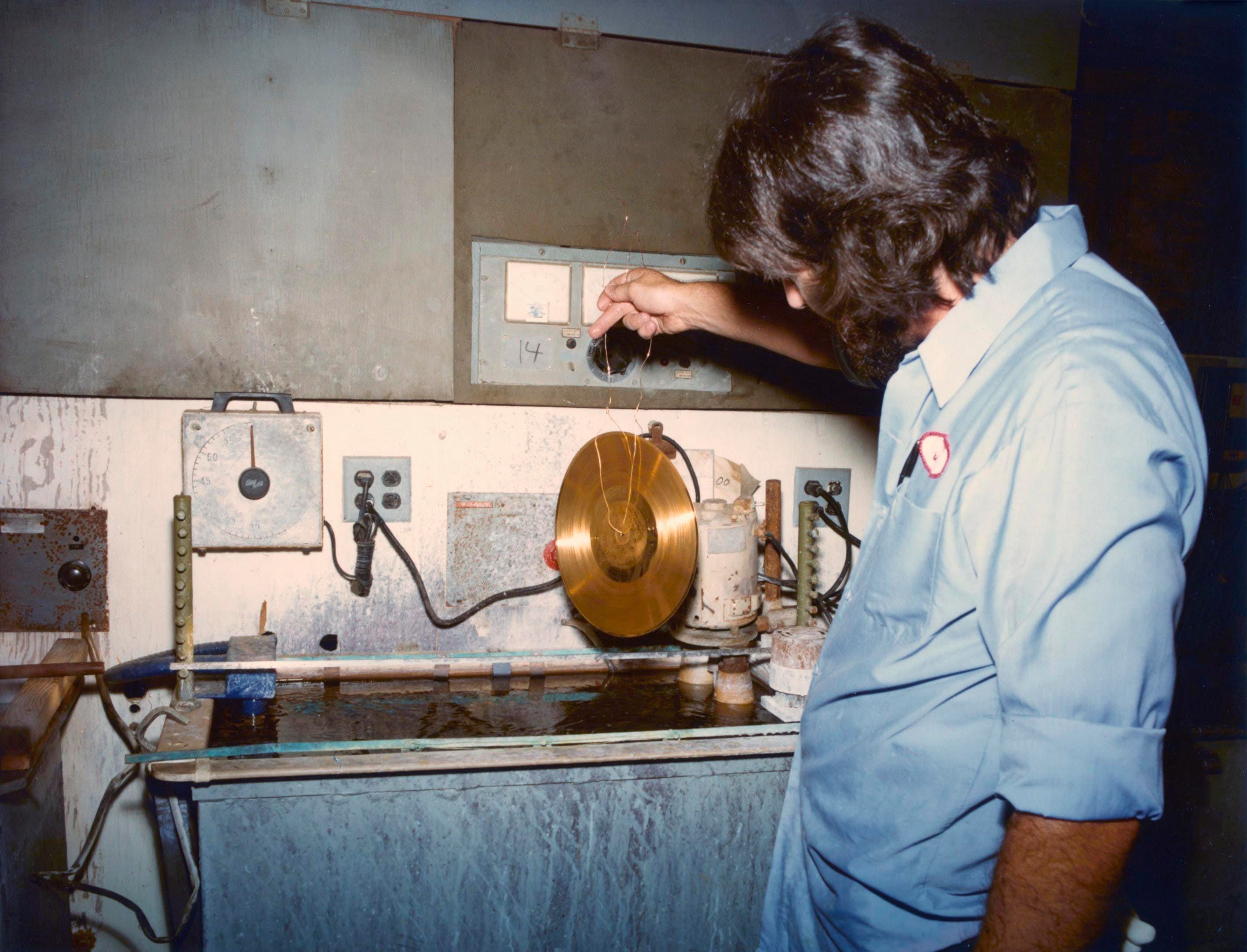 A technician dips one of the Golden Records in gold plating.