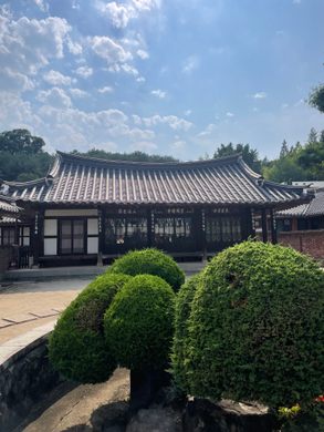 A building with a Korean style roof with trimmed green bushes in the foreground