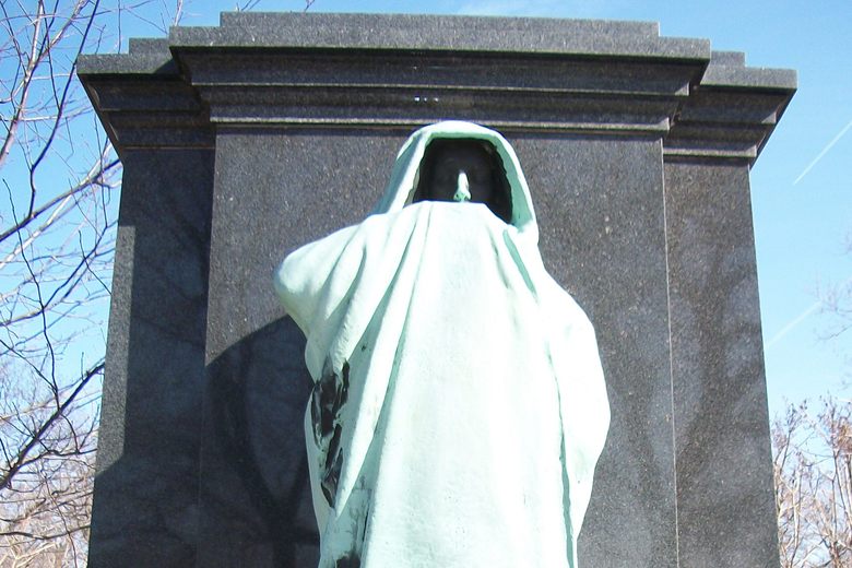 A bronze statue of a hooded, cloaked figure with its hand covering its face, set against a dark granite monument.