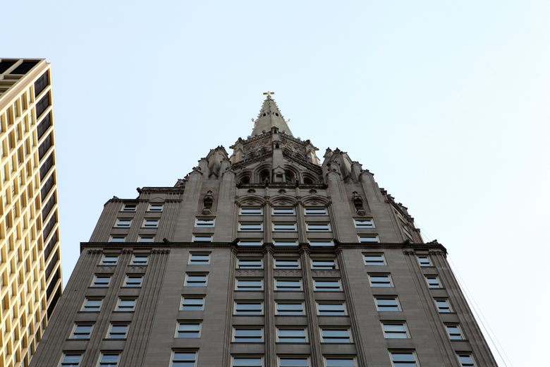 Low-angle view of the Chicago Temple Building's stone facade and gothic spire topped with a cross.
