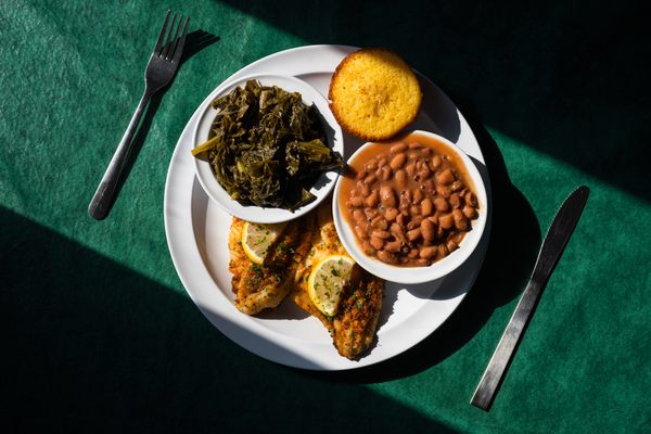 Fried catfish commands center stage on a plate with turnip greens, pinto peans, and cornbread.