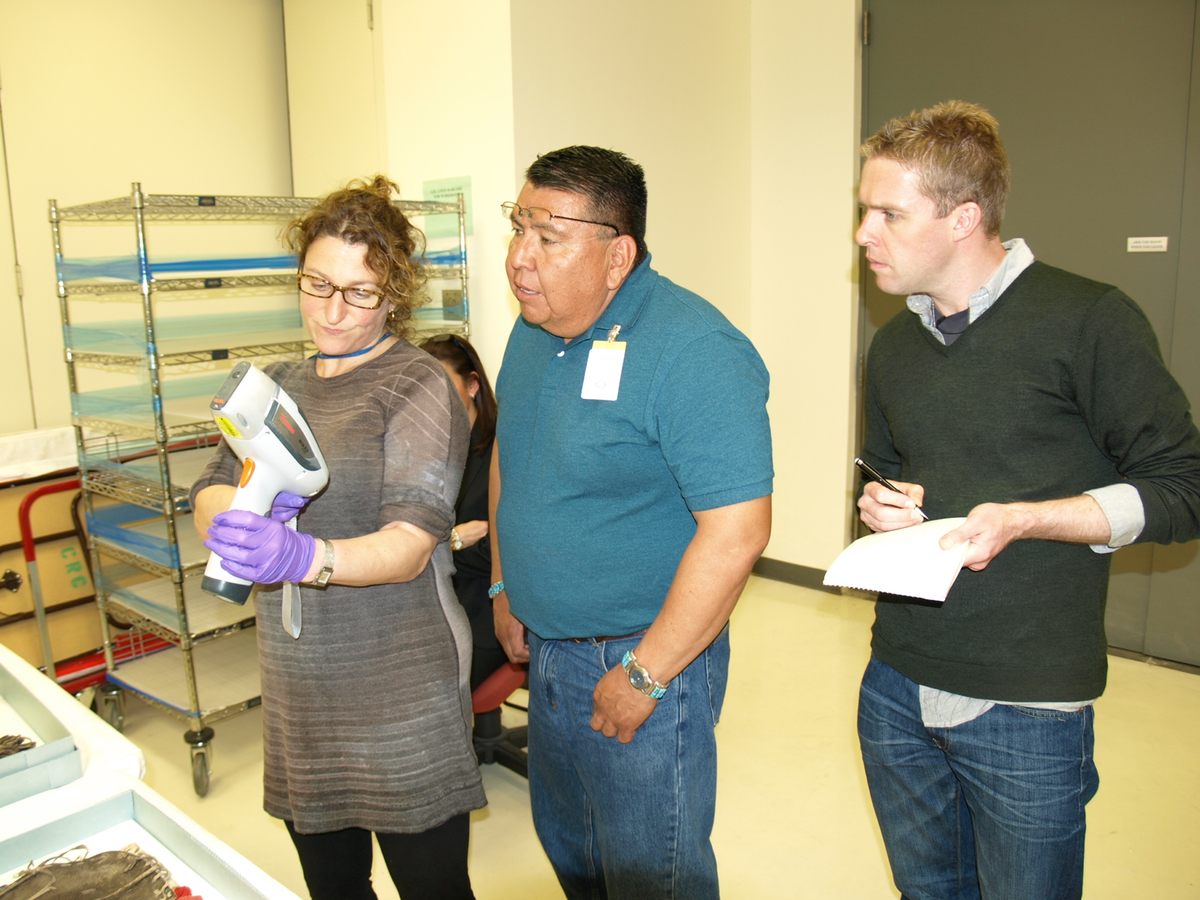 Emily Kaplan (left), a conservator at the National Museum of the American Indian, stands with Timothy Begay, a repatriation representative from the Navajo Nation, and Peter McElhinney (right), a conservation fellow at the museum. They're reviewing XRF data to determine the presence of possible pesticides.