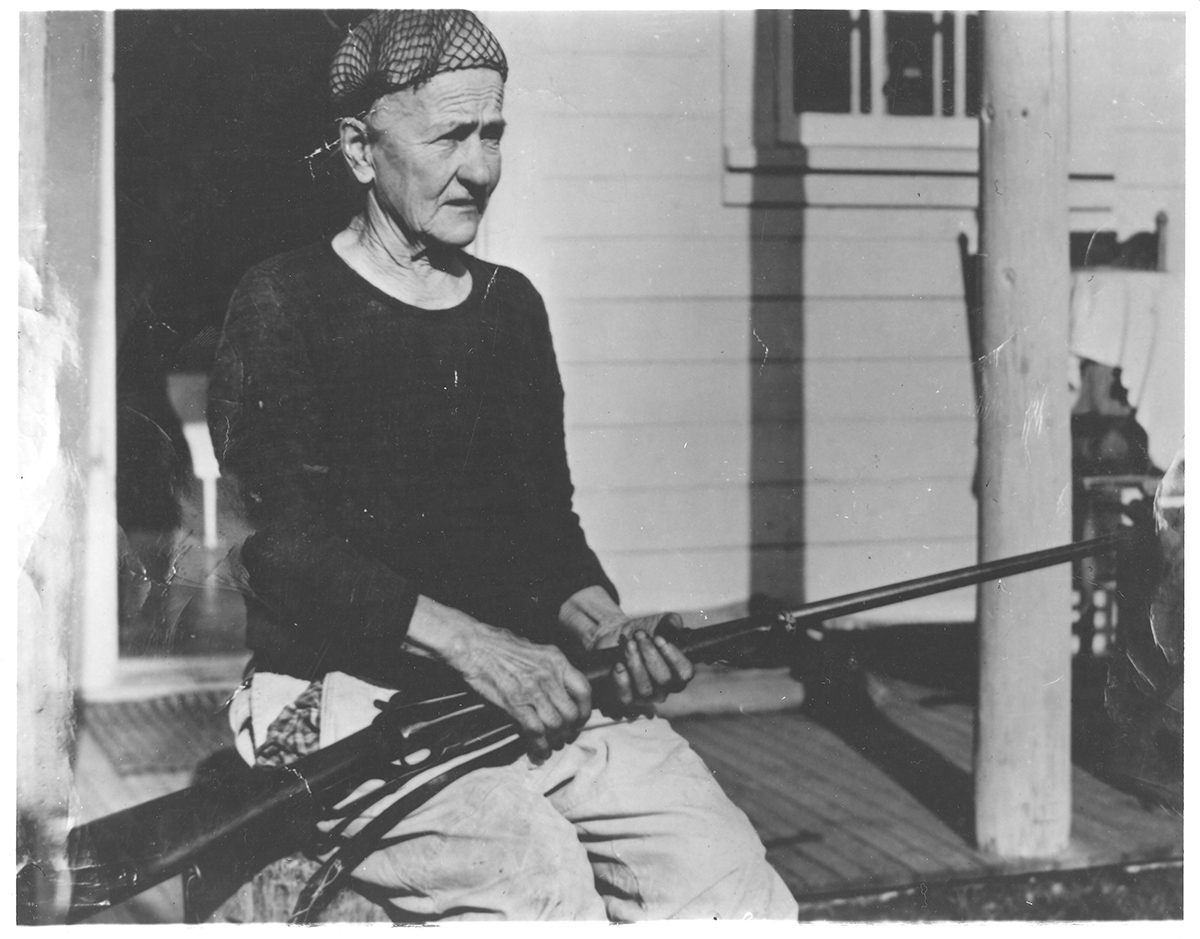 Quigley on the porch of her house in Kantishna,
holding a rifle, c. 1940