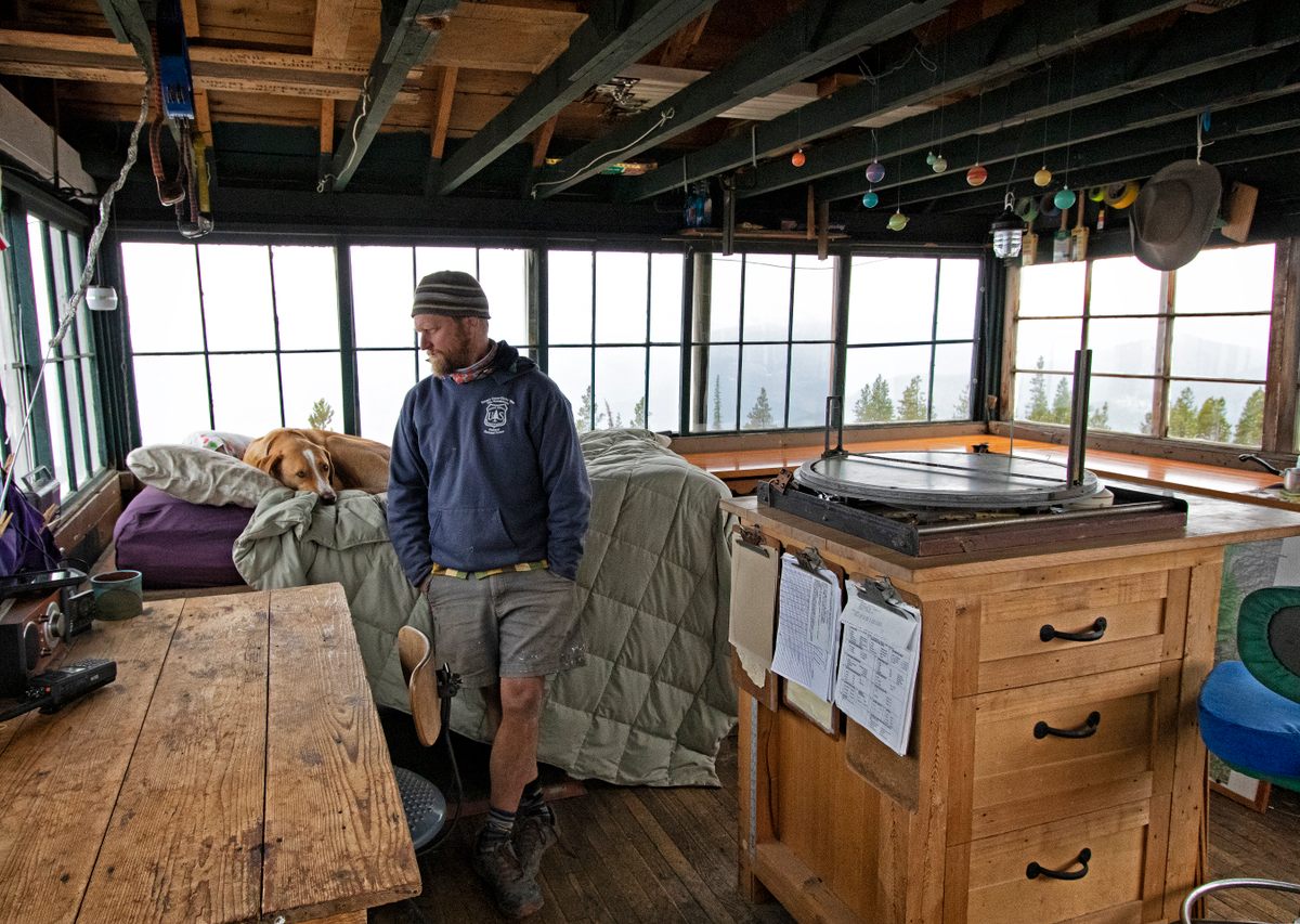 Haugen and his dog Ollie inside the Thoma Lookout in Flathead National Forest in Montana. On the right is the alidade he uses to pinpoint the location of a fire.