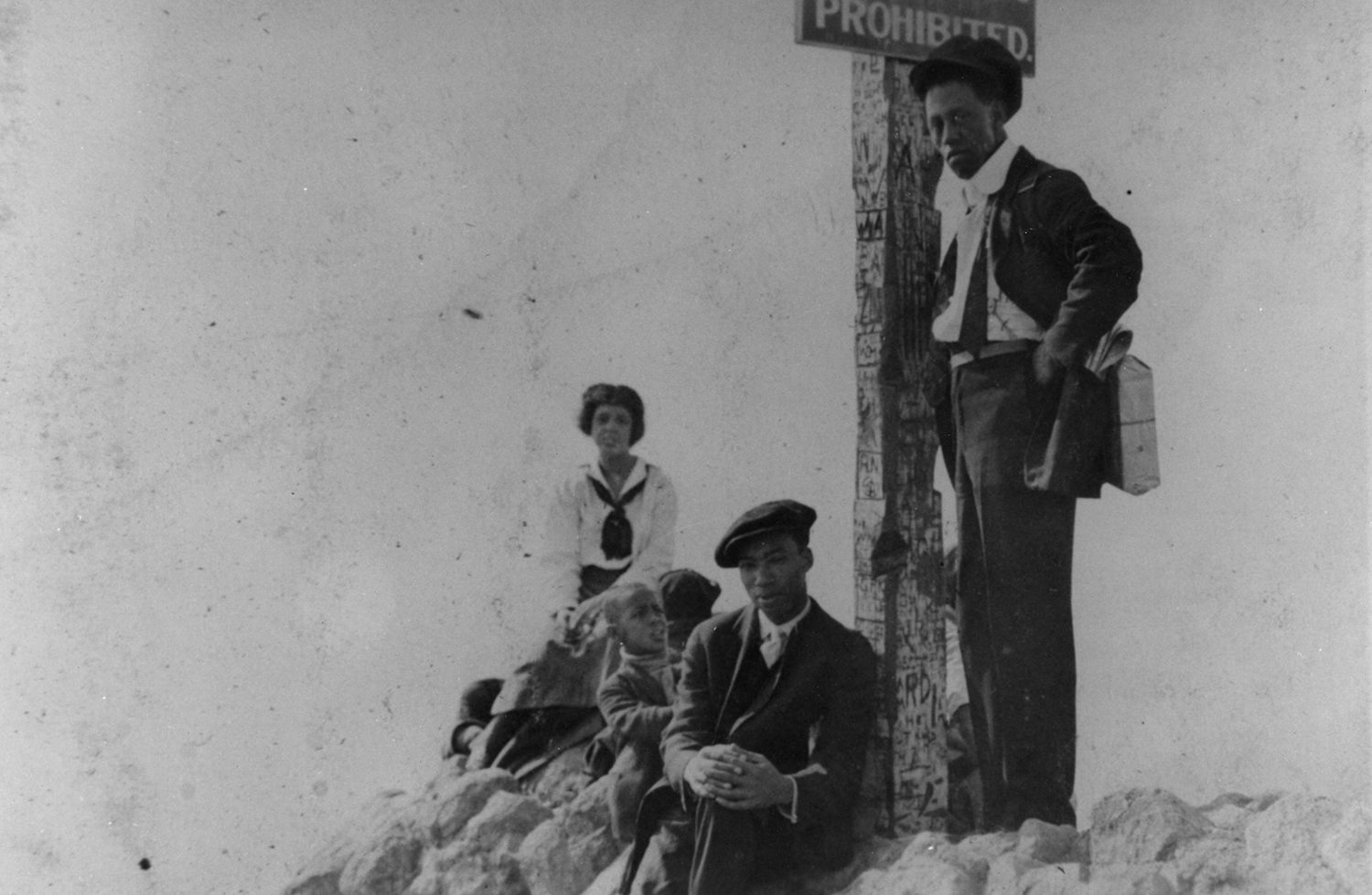 A group sits by a sign that marked the racially segregated parts of a beach in Santa Monica, ca. 1925.