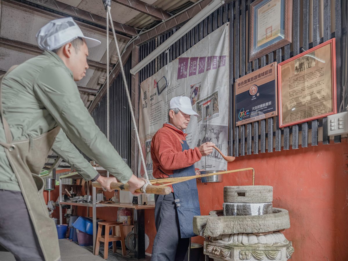 Lin Yih-Cheng, the owner of the Luoshan Organic Tofu Farm, pours soybeans into the hand-powered stone mill as his nephew, Chang Shun-Hsing works the mill.