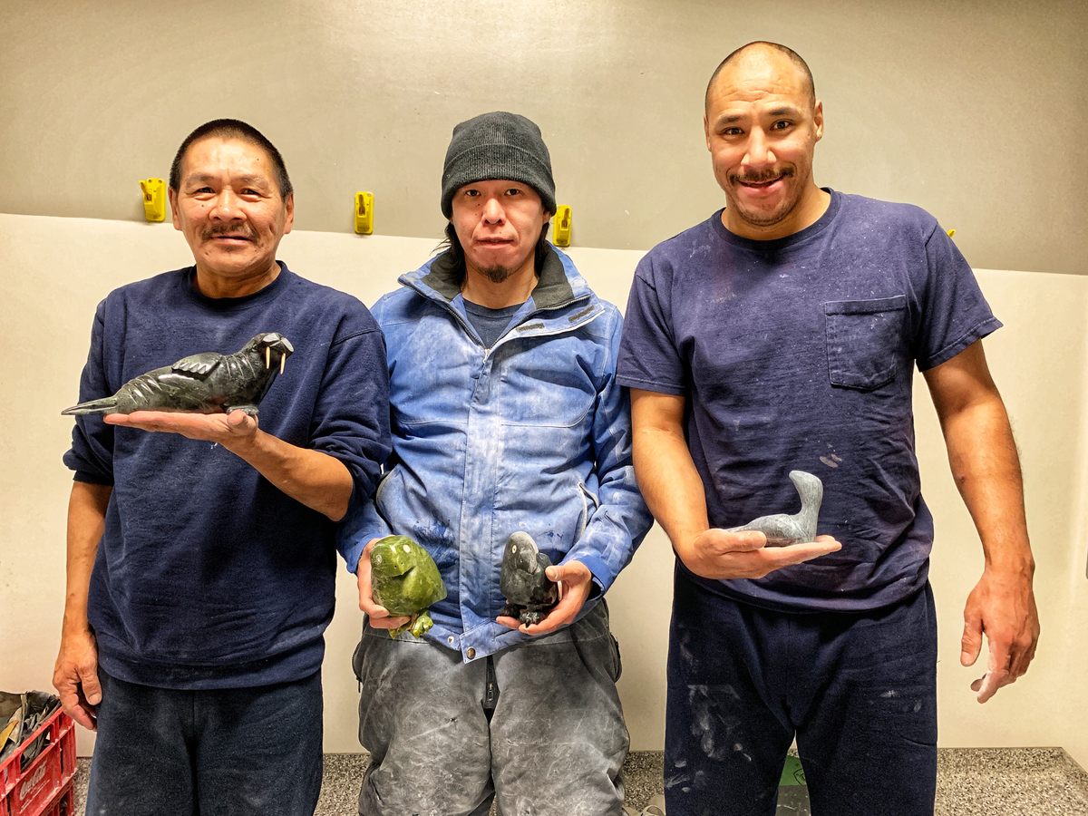 Eegeesiak Shoo, Elijah Jonah, and David Ross Pugh hold up carvings in Makigiarvik jail.