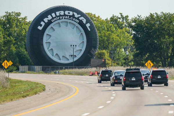 A motorcade drives past the Uniroyal Giant Tire.