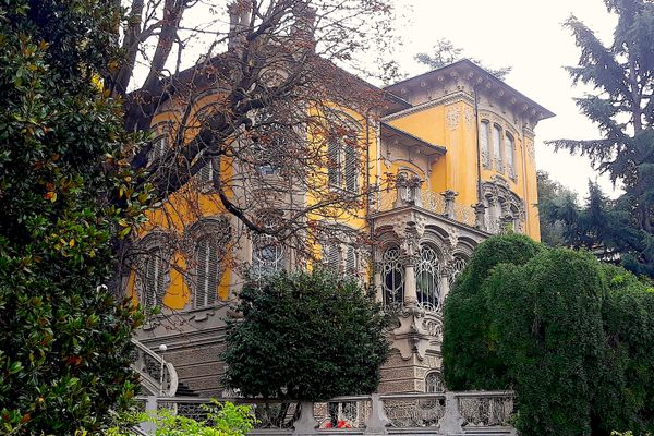 An ornate yellow Italian home peaks out behind green foliage