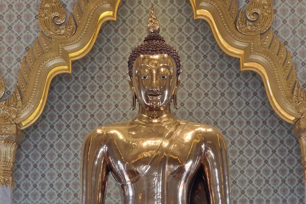Golden Buddha sits in on a marble pedestal.