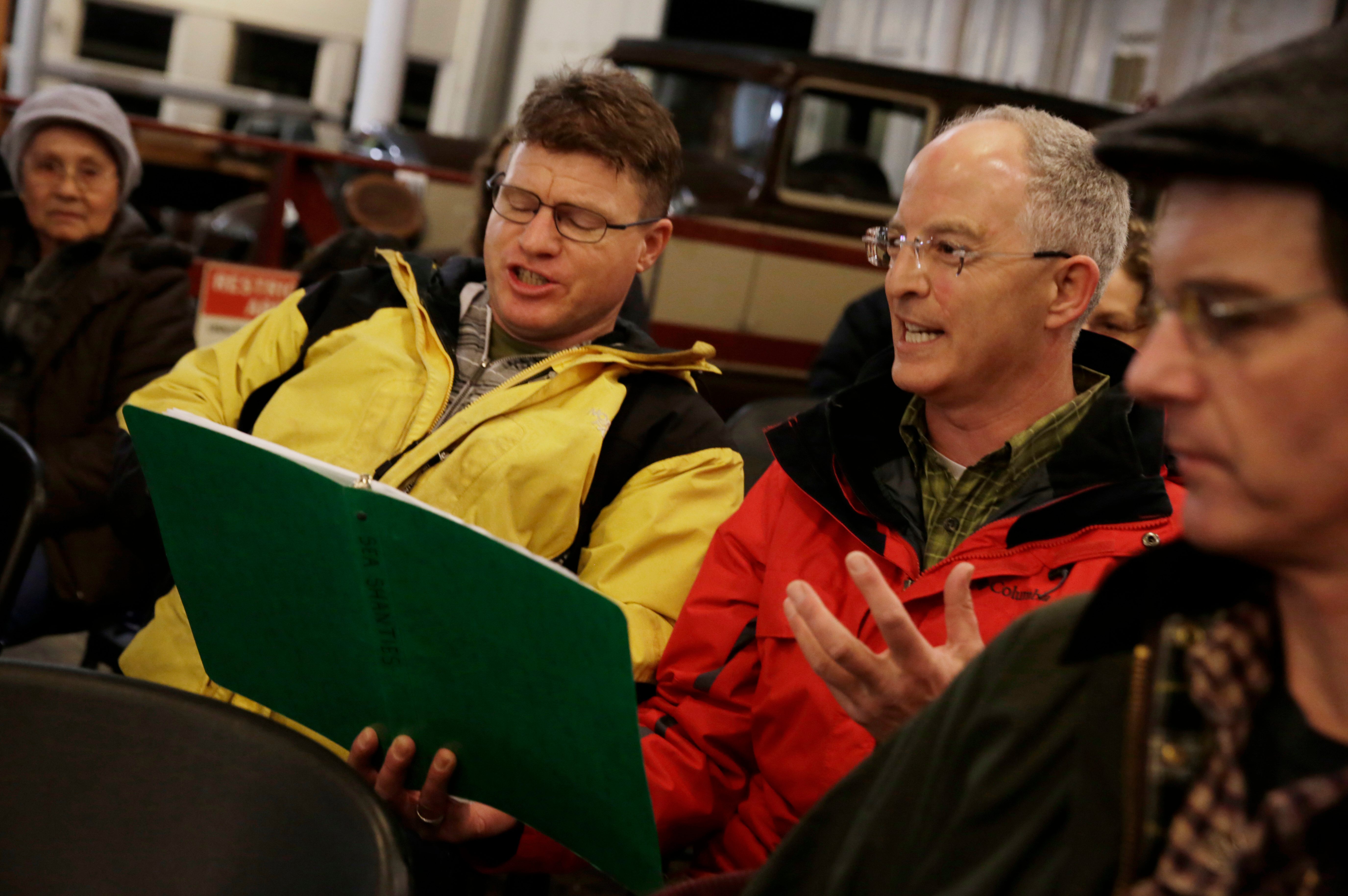 Two men hold a songbook as they lead a chantey.