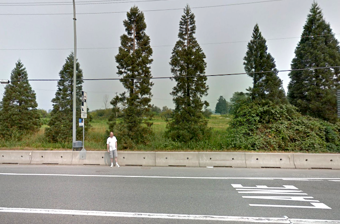 A pedestrian waits for the bus beside the Lougheed Highway.