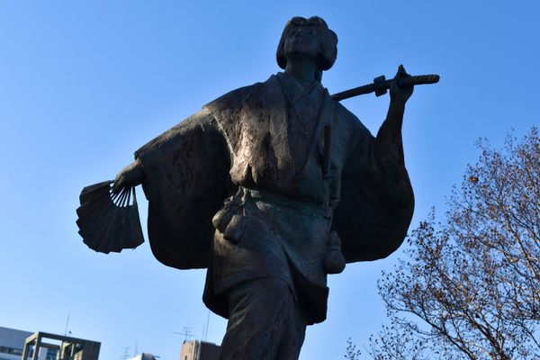 bronze statue of a woman with a samurai sword and fan in a kimono