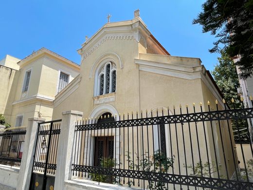 A cream-colored Greek church behind a black iron fence and gate