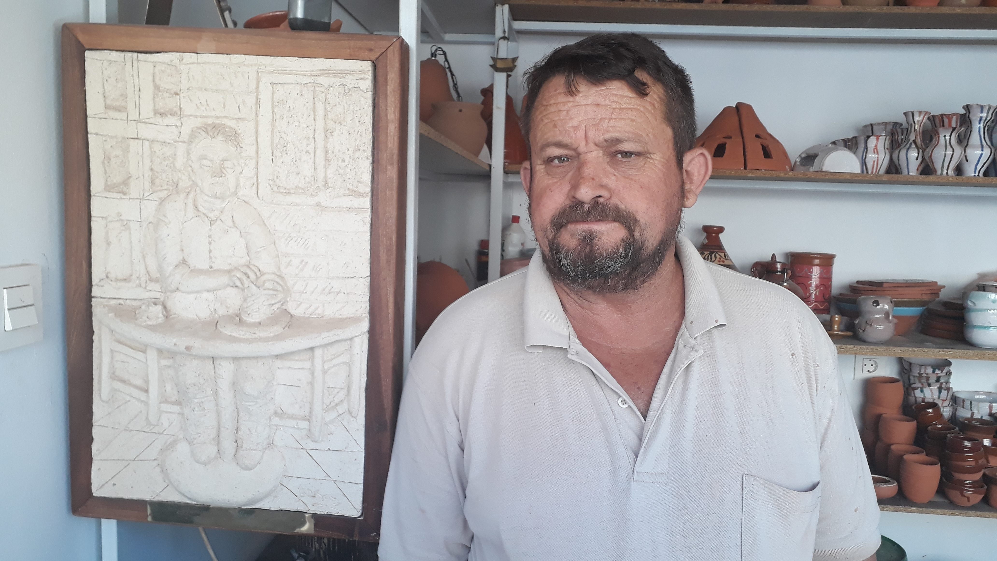 Orellana stands in his workshop, next to a drawing of his father, who was also a potter.