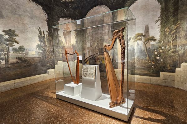 A frescoed room featuring two harps as well as a historic book opened to an illustration of a harp.