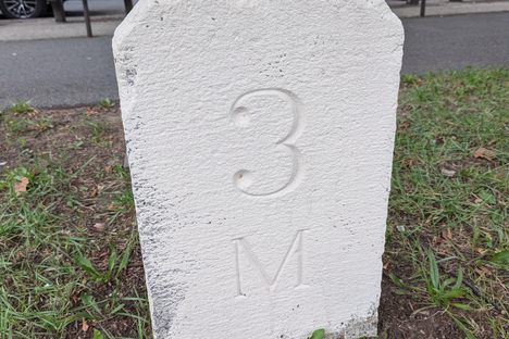 A white stone with "3M" carved into it along a bike path