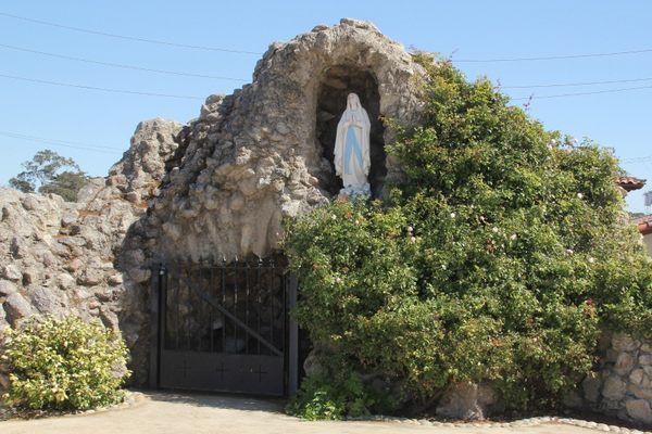A statue of Mary stands in a grotto to the left of the church