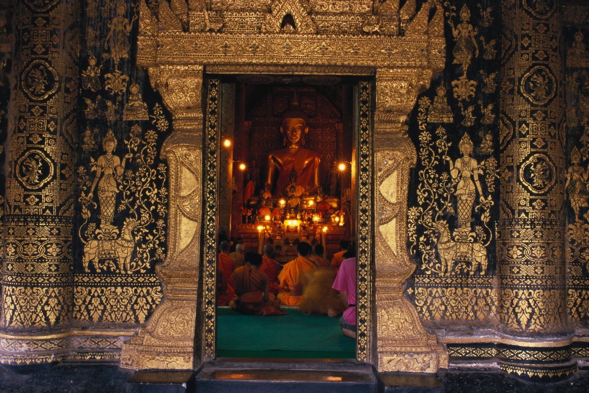 Monks sitting in front of a candlelit Buddha statue at Wat Xieng Thong temple in Luang Prabang.