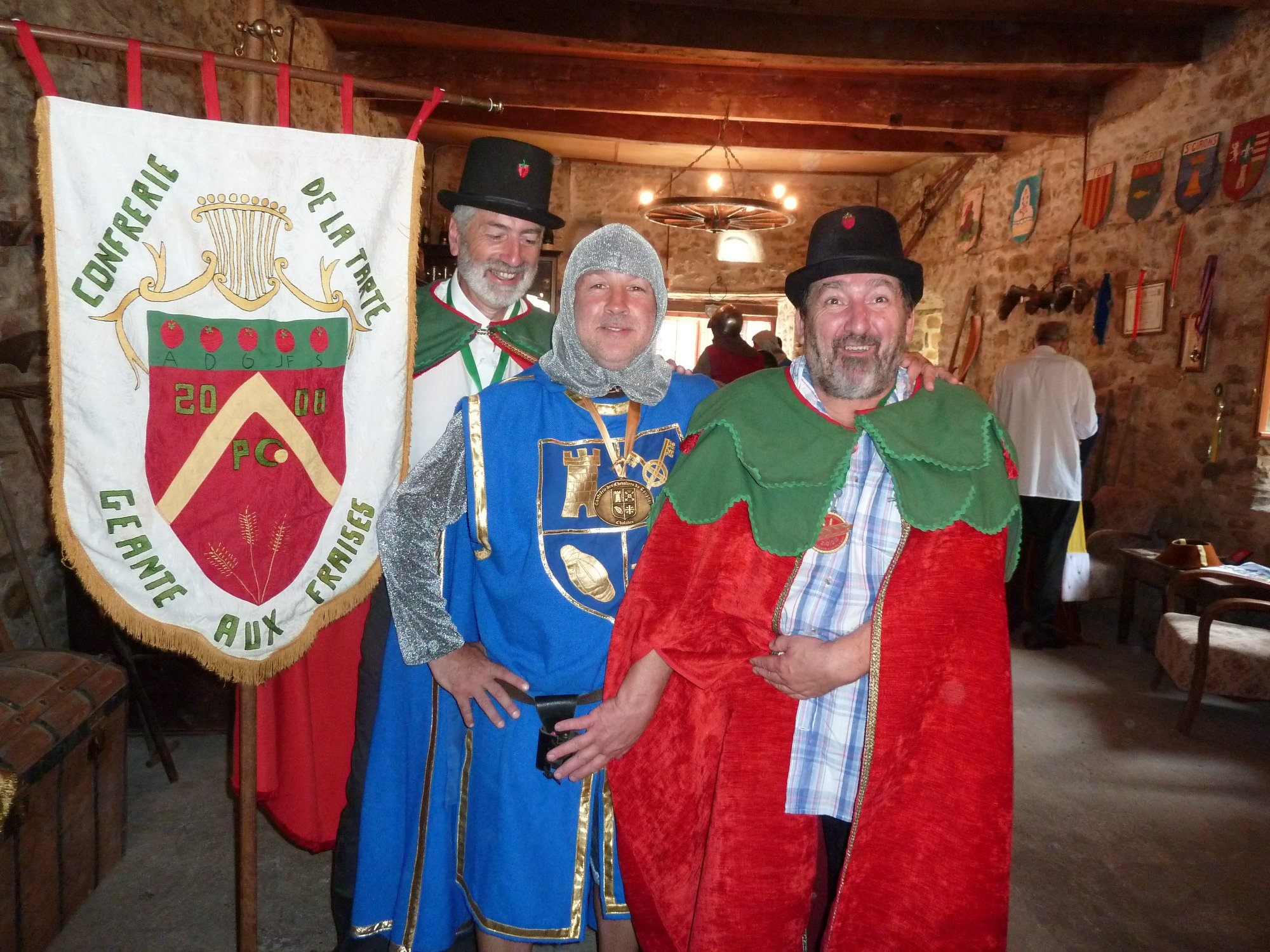 A knightly member of the La Confrérie des Chevaliers du Tougnol, along with two members of the Confrérie de la Tarte Geante Aux Fraises.