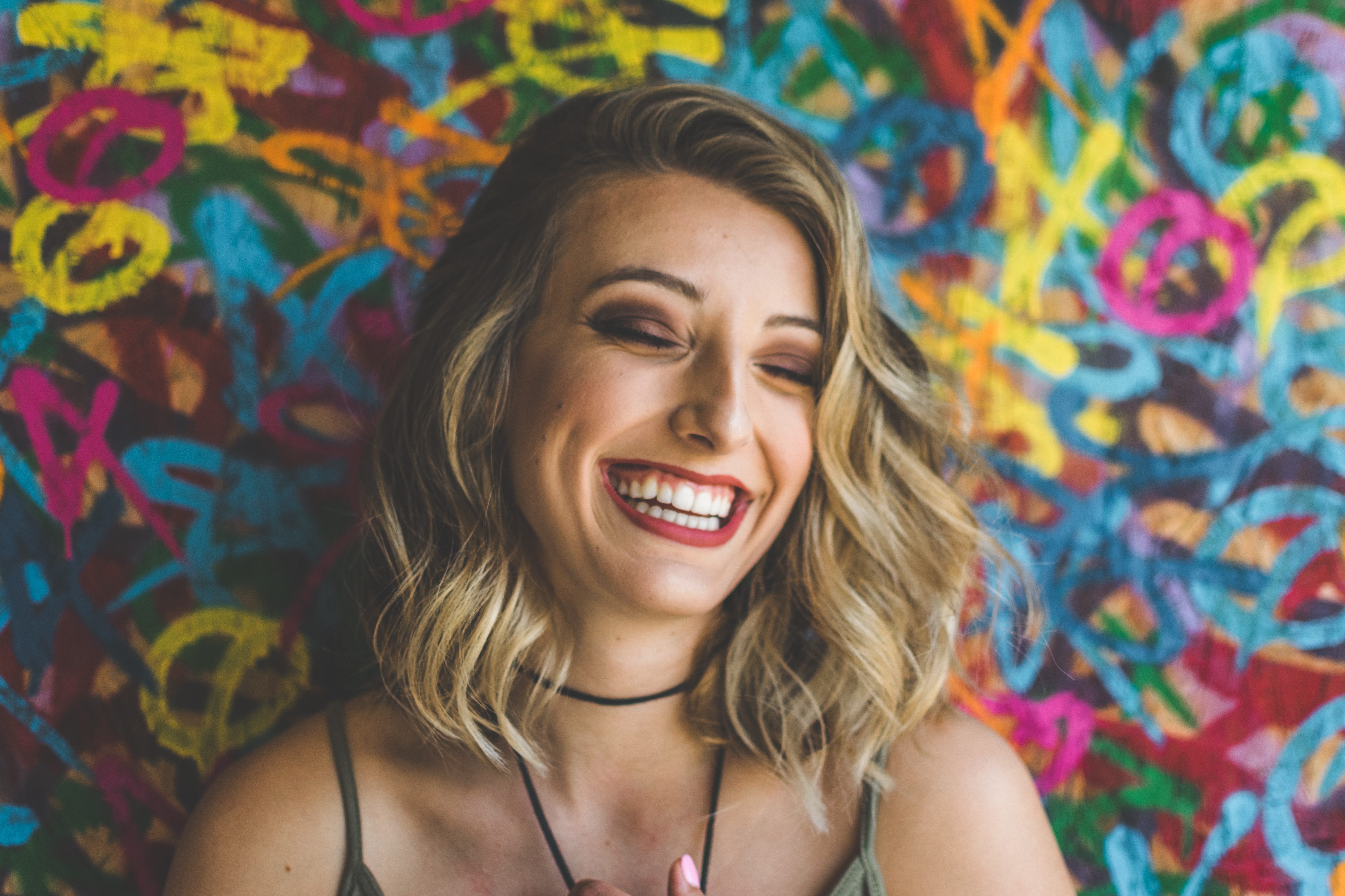 Woman laughing in front of a colorful mural. 