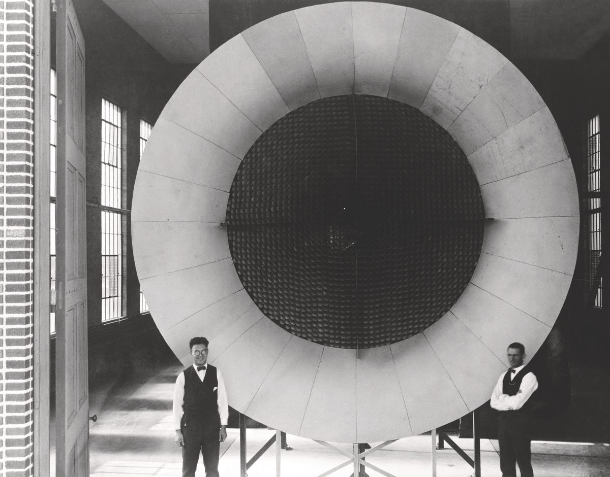 Two mechanics pose near the entrance of Langley's first wind tunnel, c. 1920.