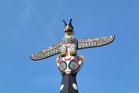 a wood-carved, painted thunderbird sits on a pole in front of a blue sky