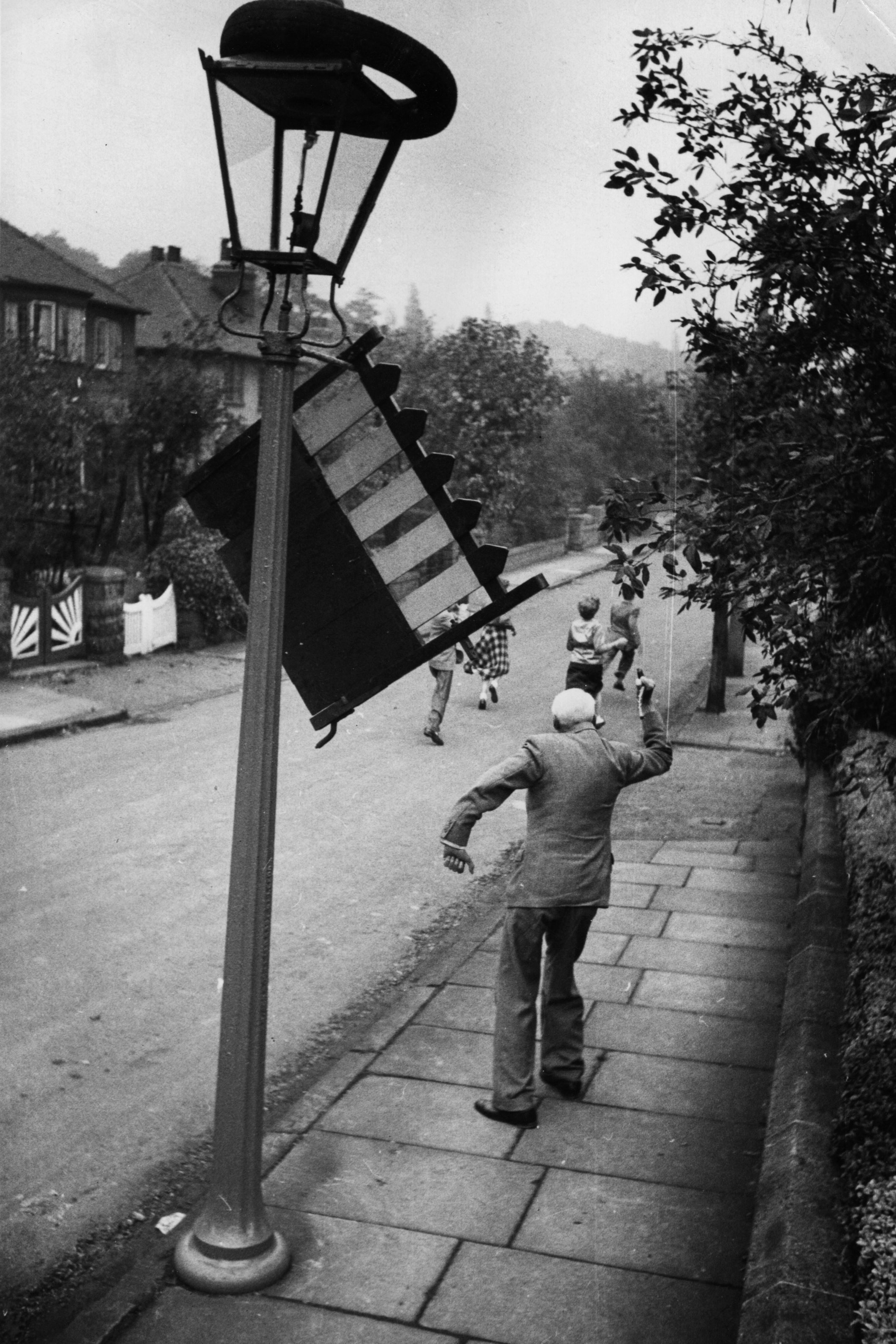 In 1954, an irate man shoos away mischief makers who hung his garden gate on a lamppost on Mischief Night in Leeds.