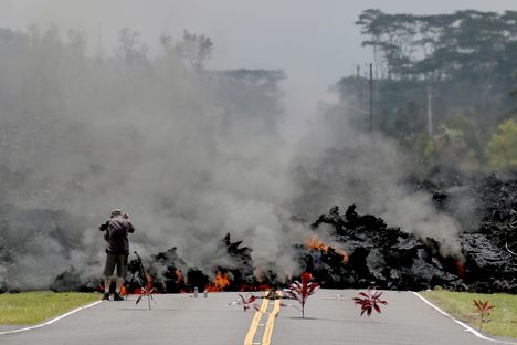 Lava burns across a road in the Leilani Estates subdivision on May 5, 2018. Offerings of Hawaiian ti leaves, rocks, and cans to the goddess Pele lie in the street in front of the lava. 