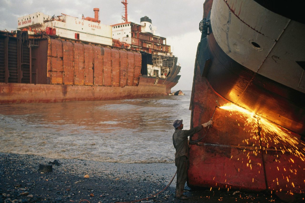 A worker uses a gas cutter to dismantle a disused vessel at Alang Shipbreaking Yard.