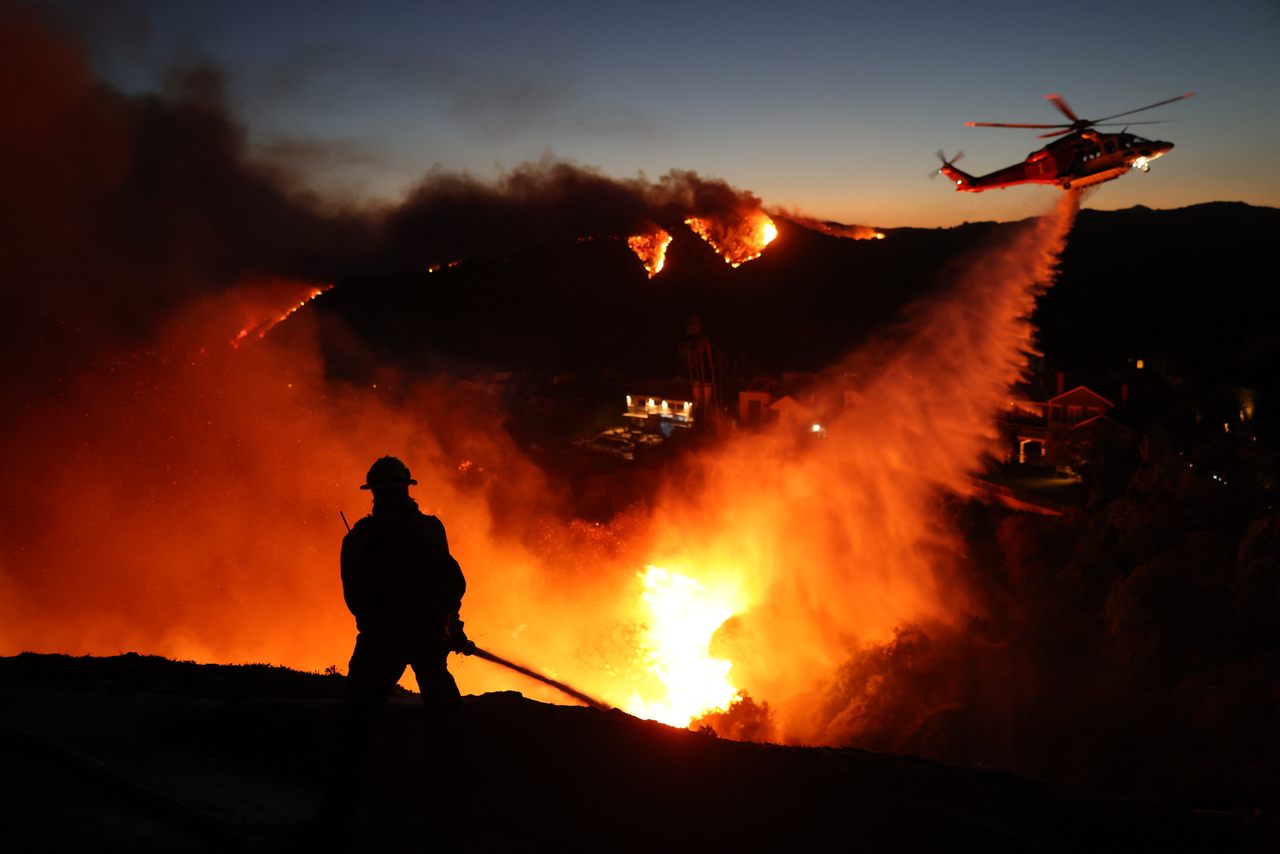 A helicopter drops water while fire personnel work on the ground to mitigate the wildfires tearing through Los Angeles, California.