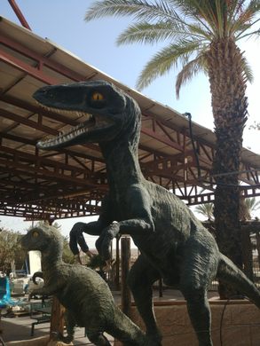 A velociraptor sculpture near a palm tree.