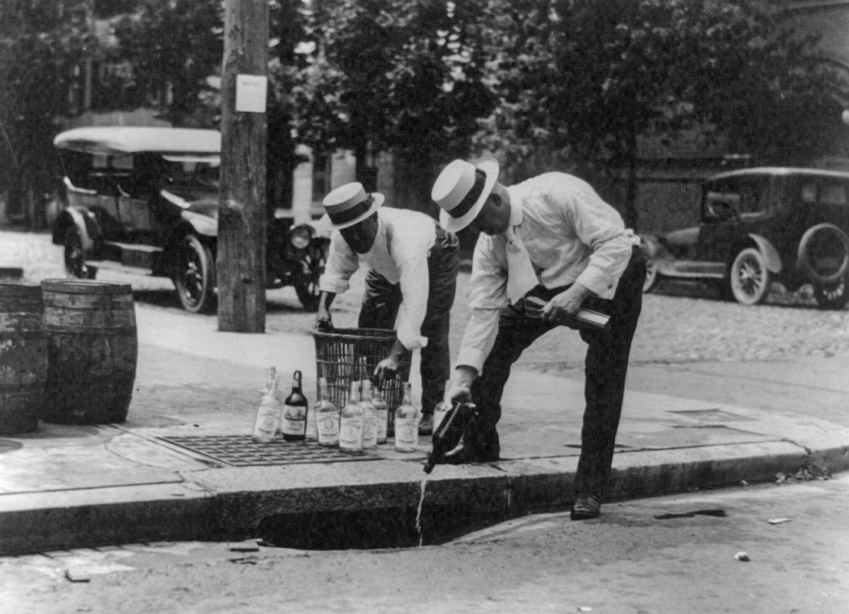Men pour whiskey into a sewer during American Prohibition.