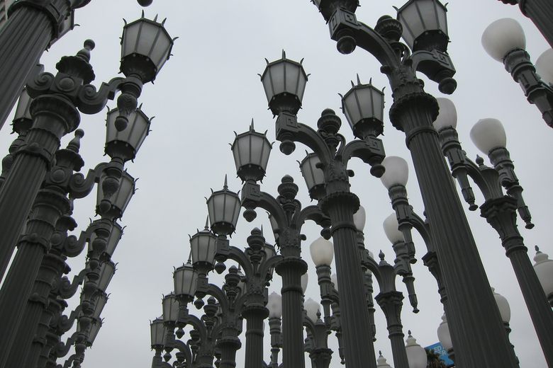A low-angle view of numerous ornate, vintage street lamps standing close together against a gray sky.