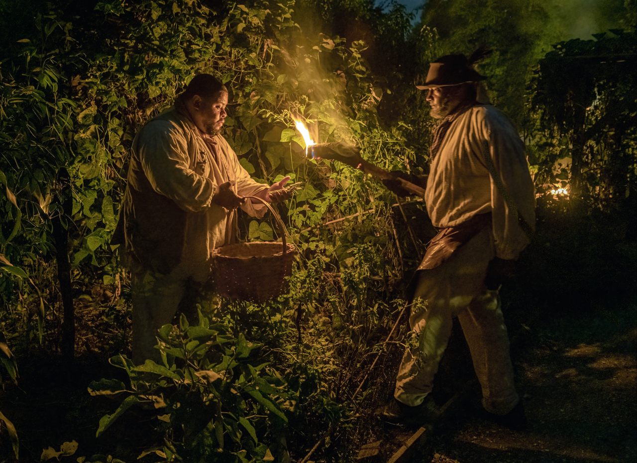 Culinary historian Michael Twitty (left) and interpreter Robert Watson pick case-knife beans by torch light at the Sankofa Heritage Garden.