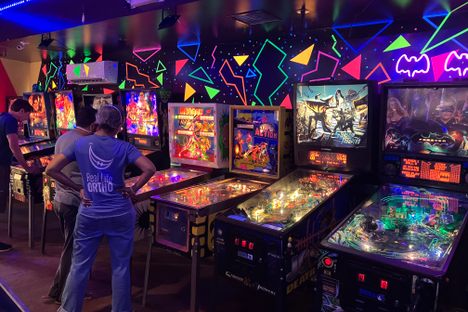 A blacklight- and neon-lit wall of pinball machines at Seven's Pinballorama