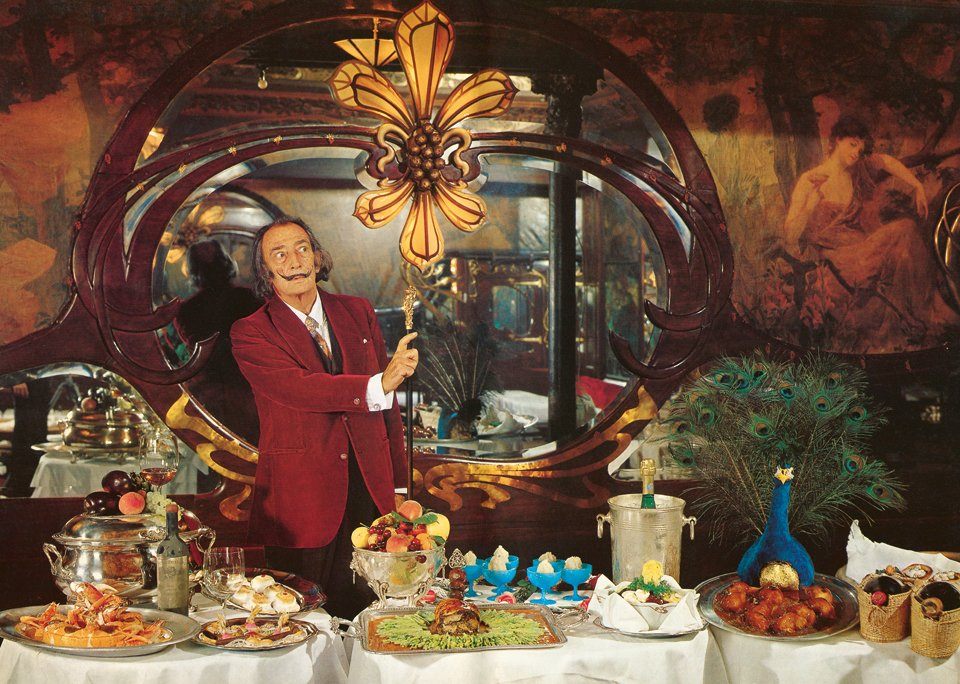 Salvador Dali at one of his lavish dinners. Some of the dishes featured in the photograph appear in his cookbook, <em>Les Dîners de Gala</em>. 
