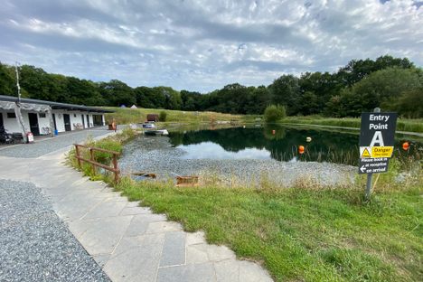 a small lake along a stone path next to a small one-story white building surrounded by grass