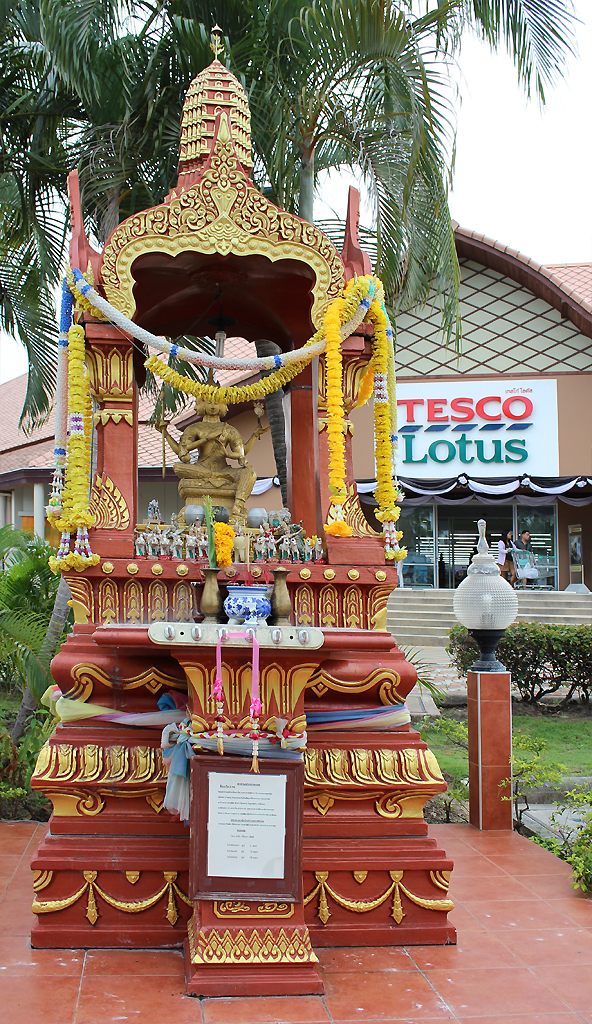 A spirit house to Phra Phrom stands tall in front of a Tesco Lotus.