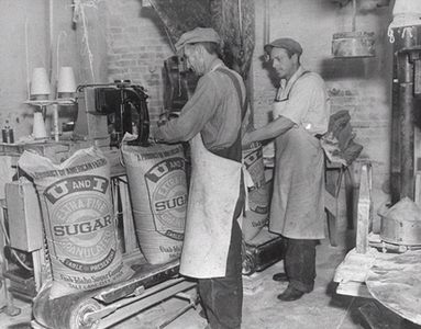 Workers sew sacks of refined U and I sugar.