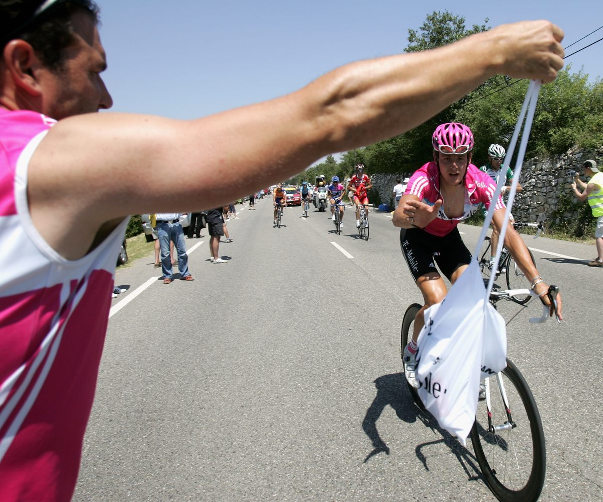 A good soigneur holds the bag high enough that the rider can grab the strap close to where it meets the bag and follows the rider’s movement with their arm.