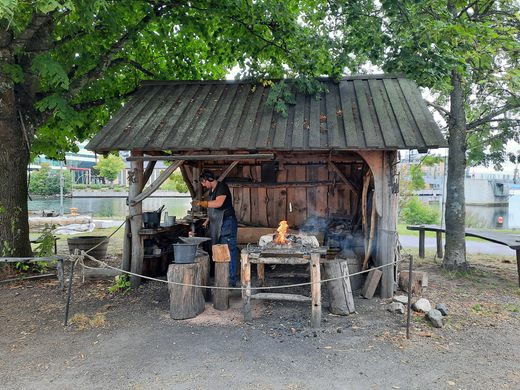 A wooden hut where a blacksmith works under a tree.